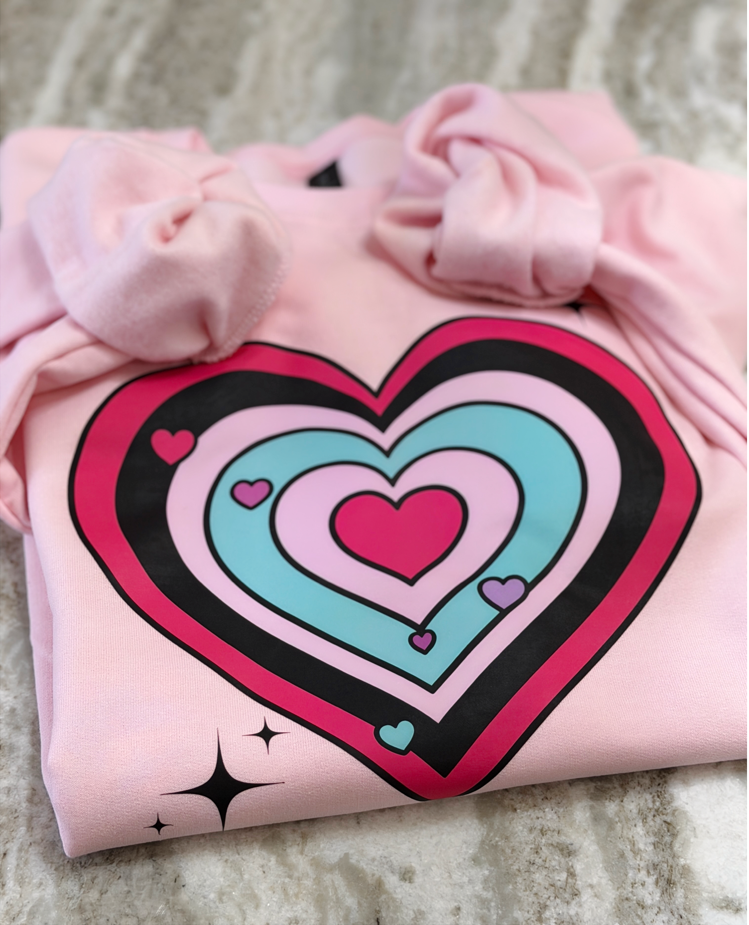 Pink sweatshirt with a colorful heart design on a textured surface