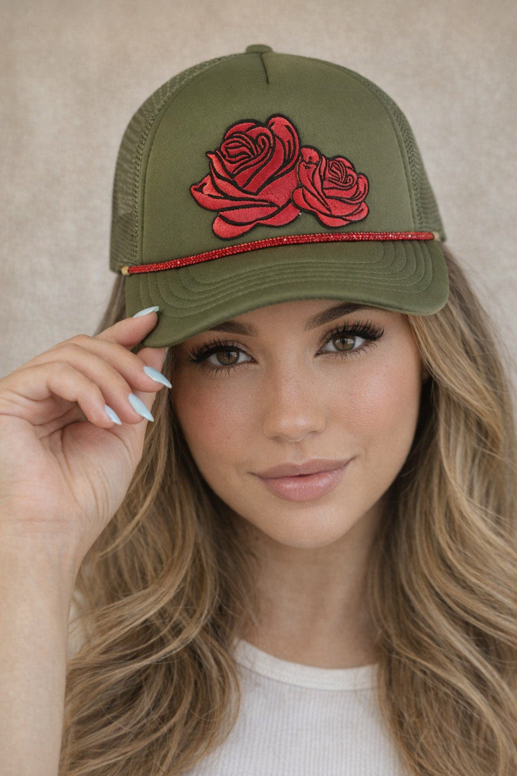 Woman wearing a green cap with red rose design against a neutral background