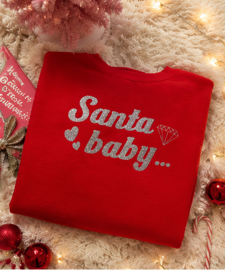 A folded red crewneck sweatshirt with 'Santa baby.