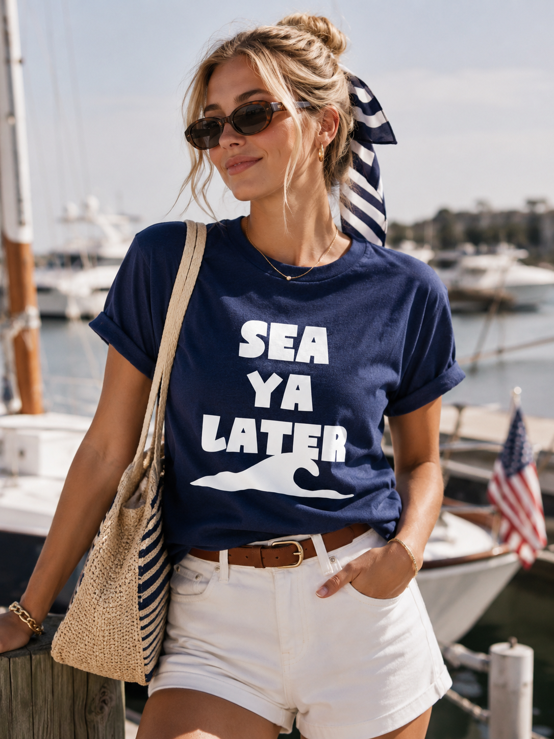 Woman wearing a navy blue t-shirt with 'SEA YA LATER' text and white shorts, standing by a marina.