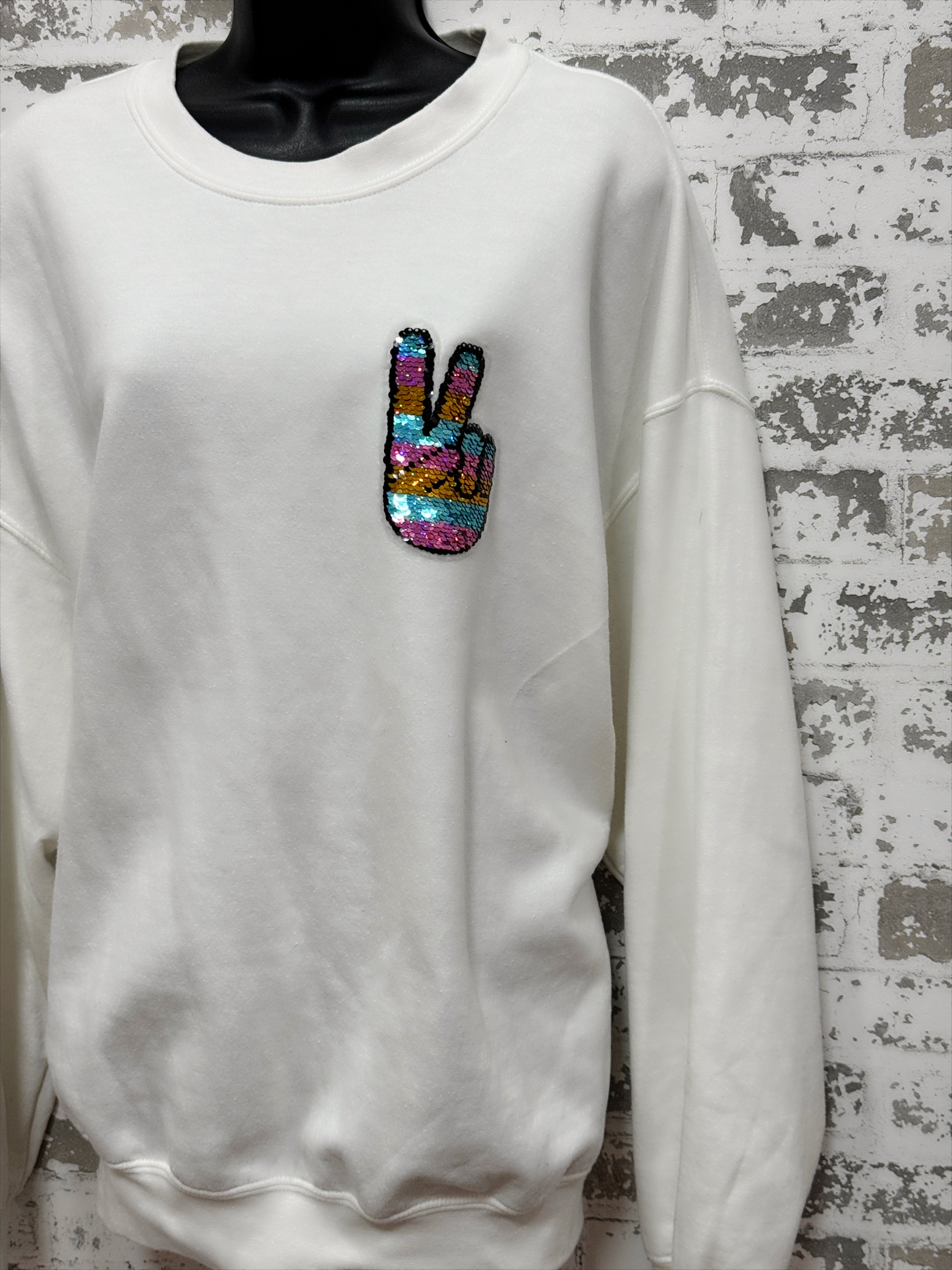 White sweatshirt with a colorful peace sign patch on a textured wall background