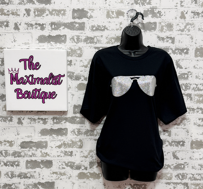 Black t-shirt with a graphic design on a mannequin against a textured wall with 'The Maximalist Boutique' sign.