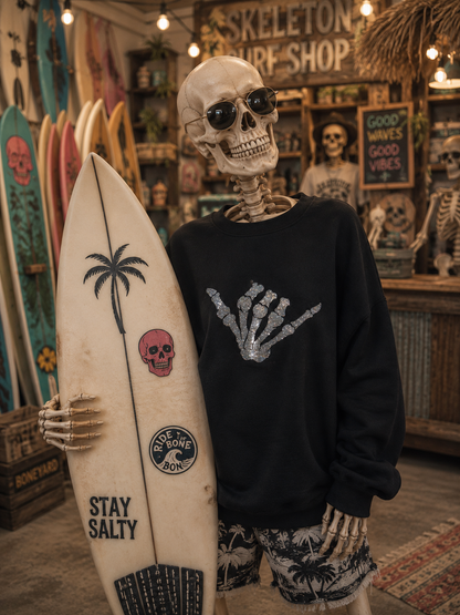 Skeleton wearing a black sweatshirt with a glitter skeleton hand shaka 