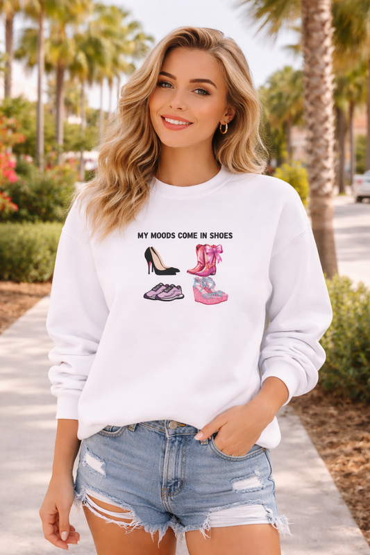 Woman wearing a white sweatshirt with shoe designs and text, standing outdoors.