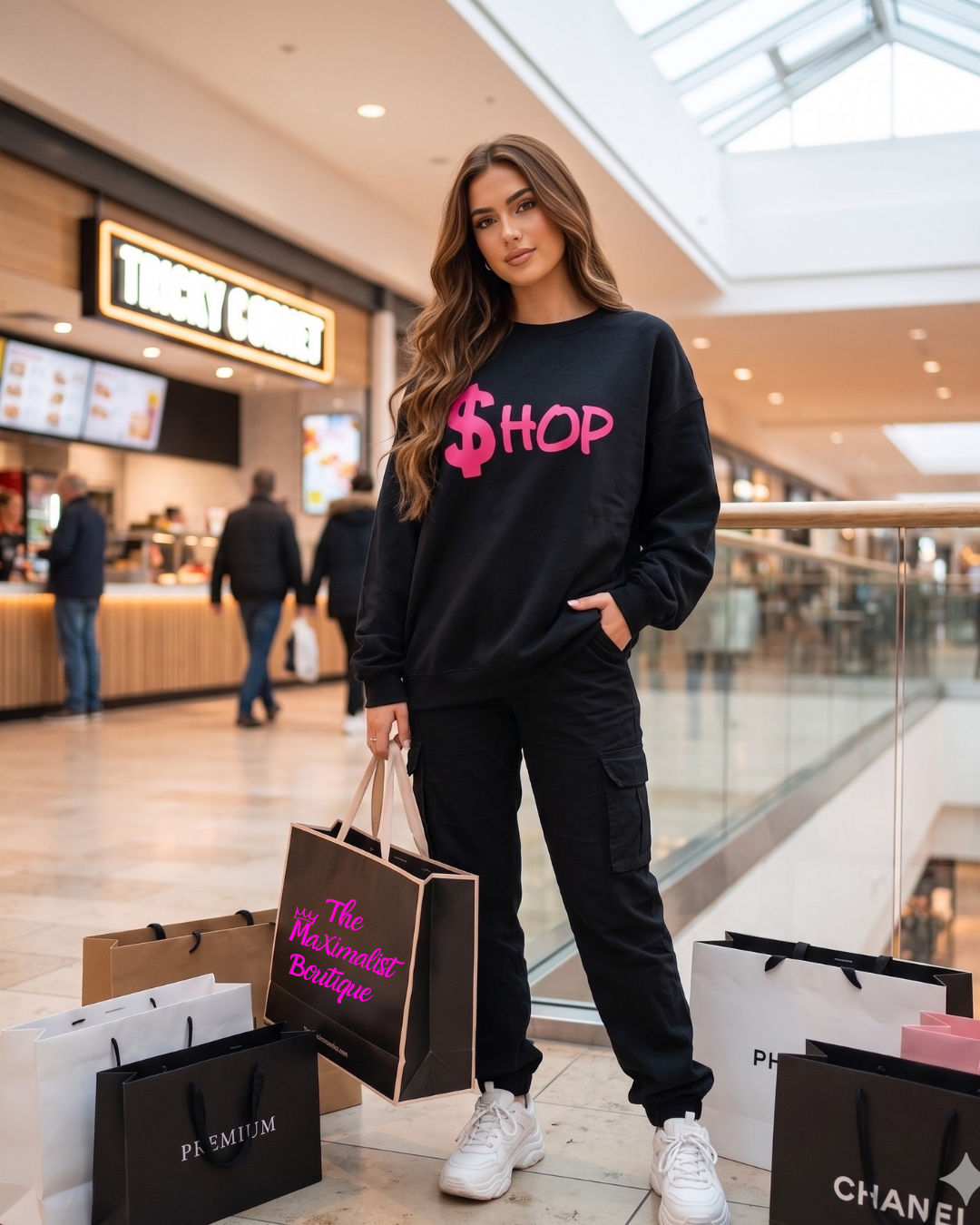Woman in a black sweatshirt with pink text, surrounded by shopping bags in a mall.