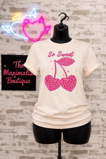 Natural t-shirt with pink graphic design on a mannequin against a brick wall with neon sign.