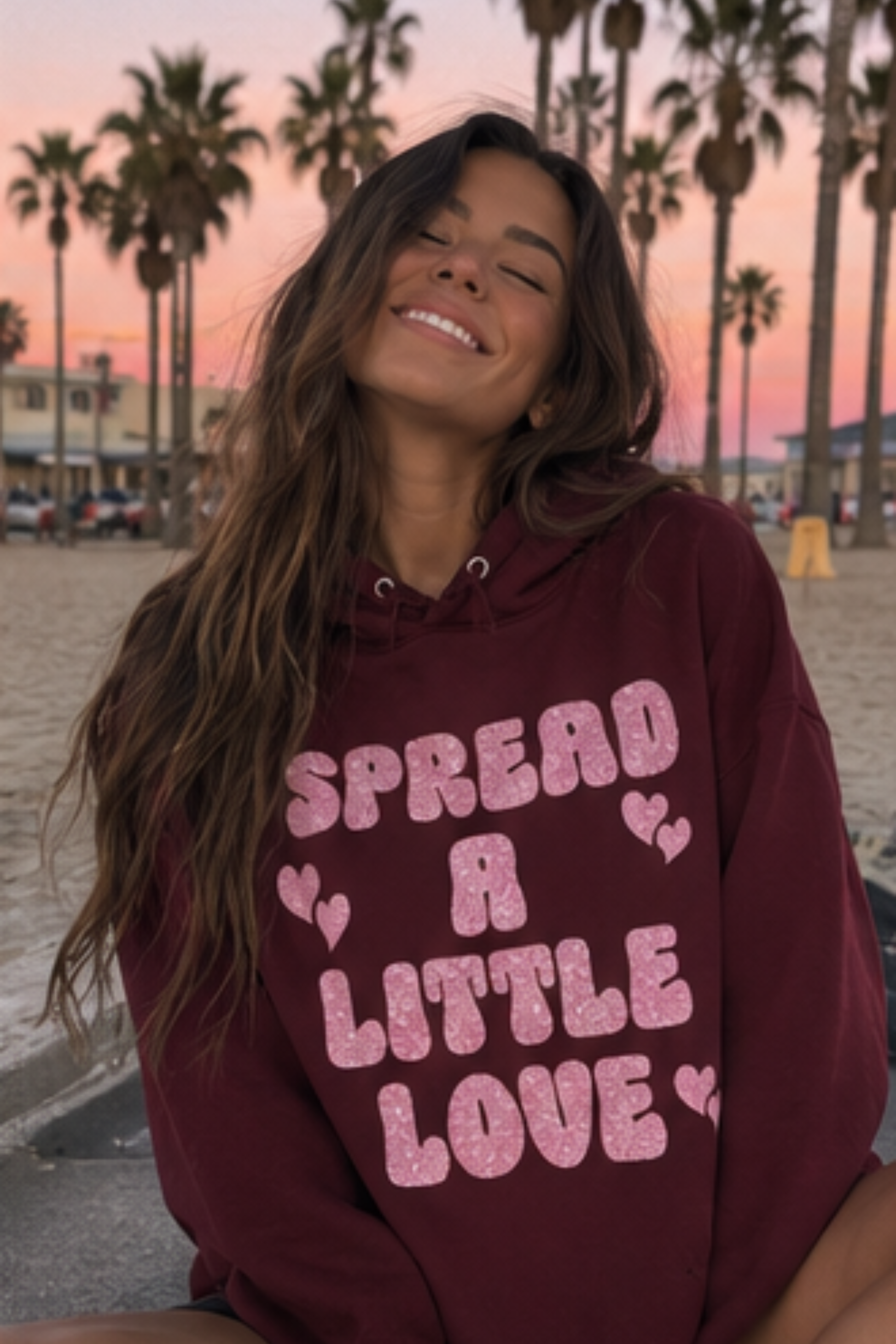 Woman wearing a maroon sweatshirt that says "Spread A Little Love" in a pink glitter graphic with hearts.