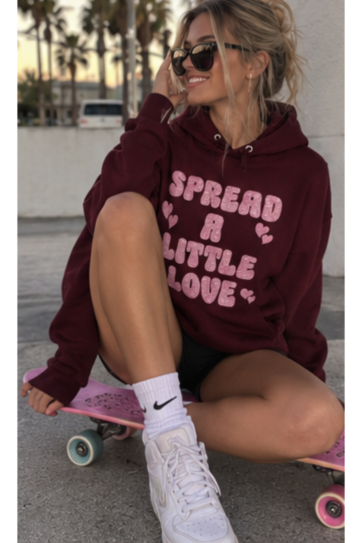 Woman wearing a maroon sweatshirt that says "Spread A Little Love" in a pink glitter graphic with hearts.