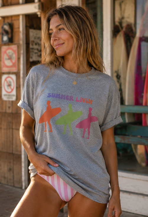 Woman wearing a gray t-shirt with colorful graphic designs in front of a store with surfboards.
