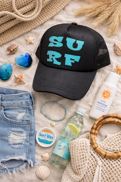 Black cap with 'SURF' text on a beach setting with sunglasses, sunscreen, and other beach accessories.