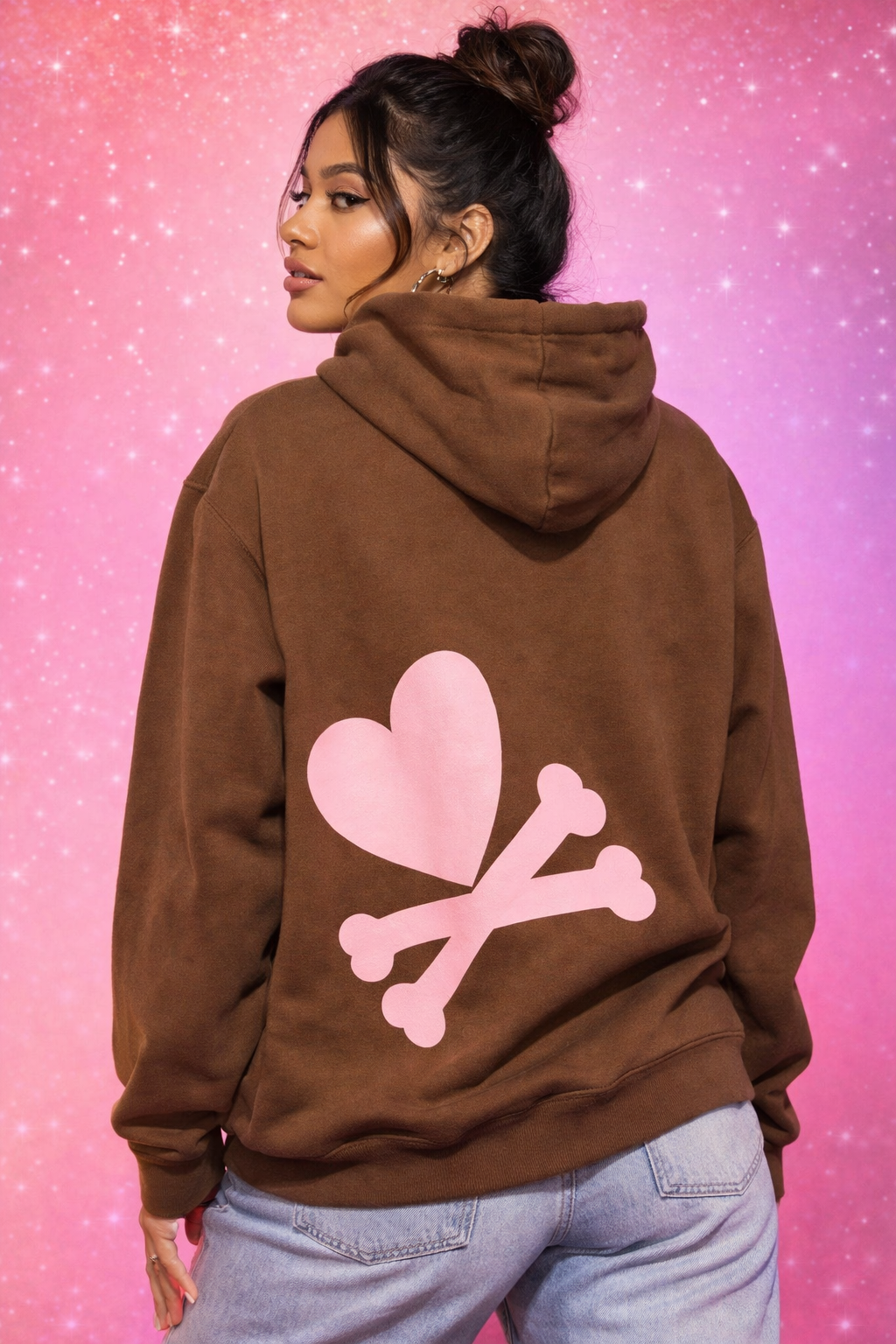 Person wearing a brown hoodie with pink heart and bone design on a pink gradient background