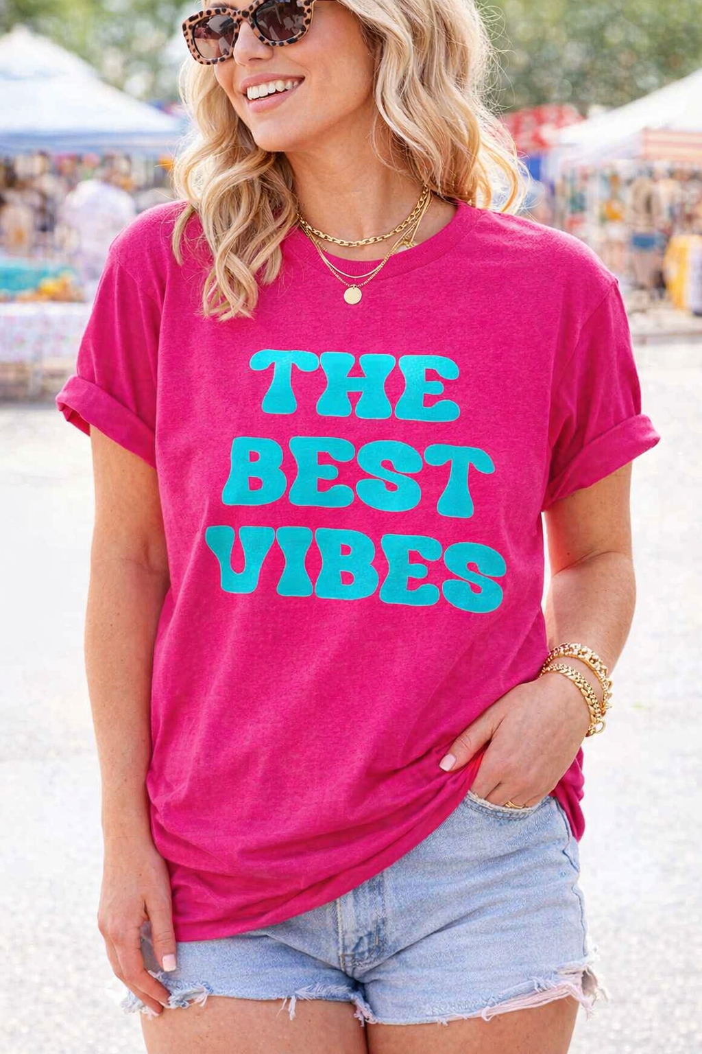Woman wearing a pink t-shirt with 'The Best Vibes' text at an outdoor event.