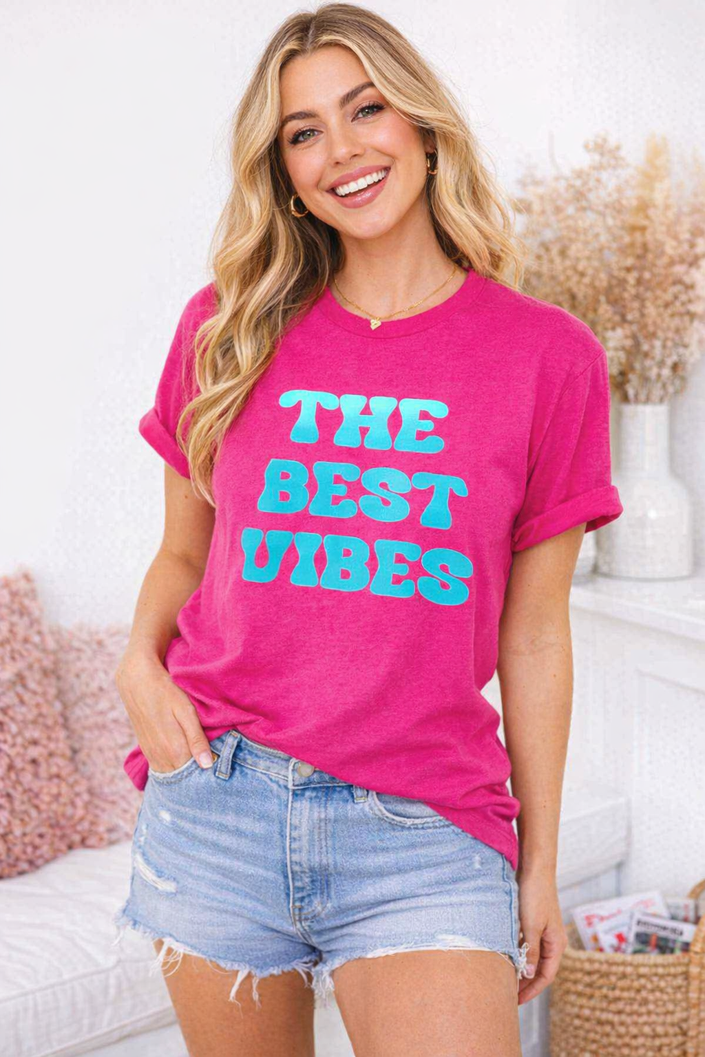 Woman wearing a pink t-shirt with 'The Best Vibes' text in a casual setting.