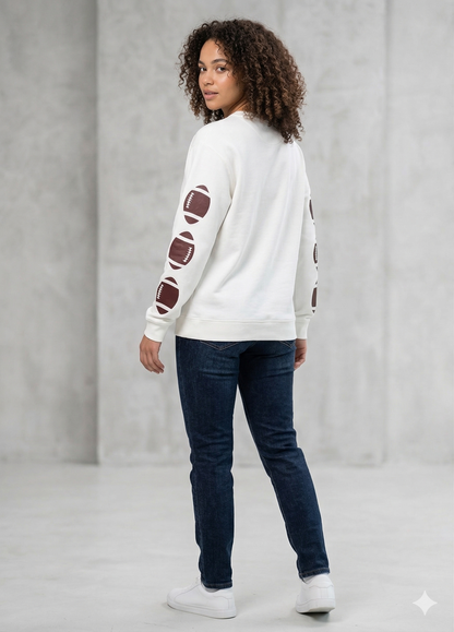 Person wearing a white sweater with football designs on sleeves against a gray background
