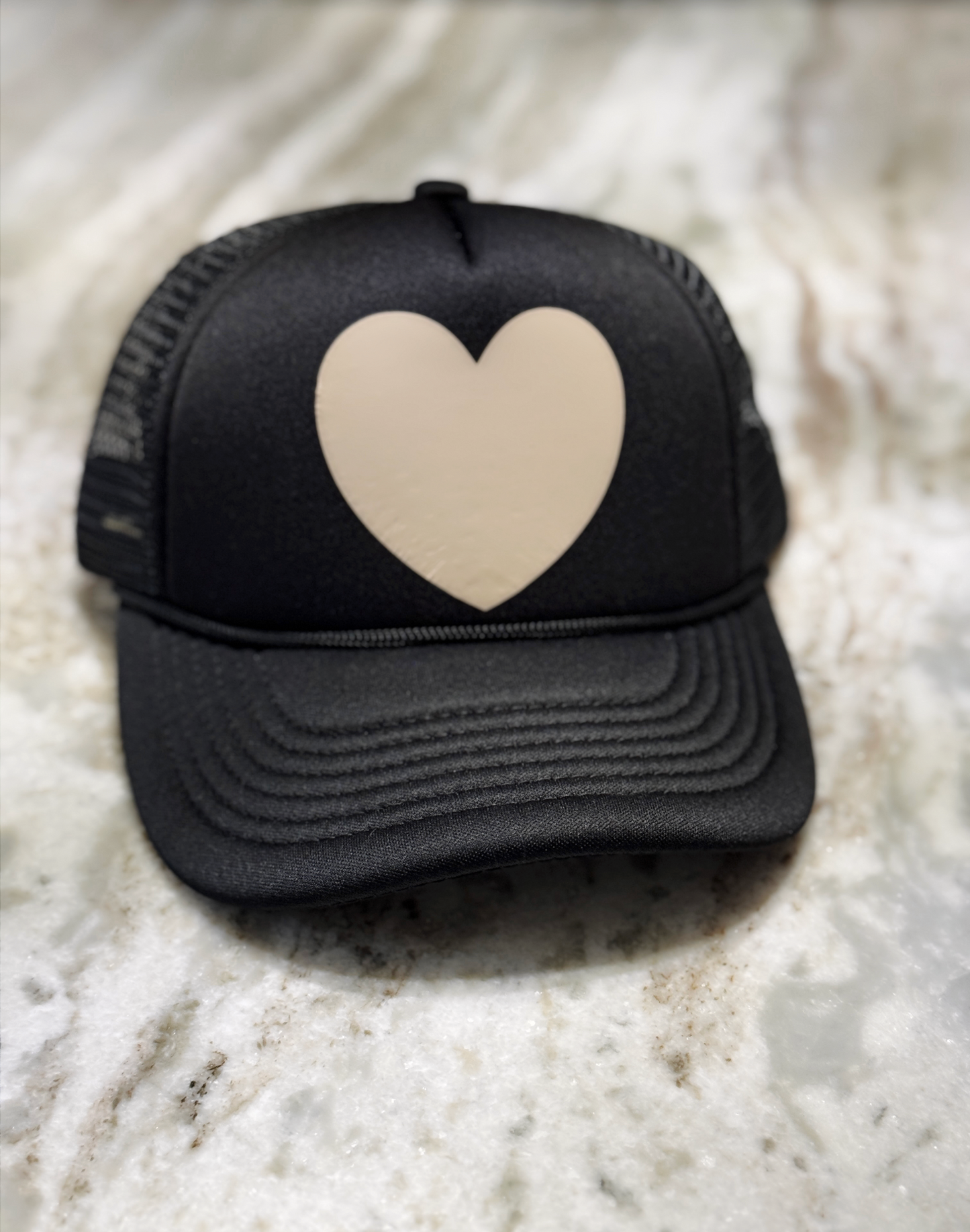 Black cap with a beige heart on a marble surface