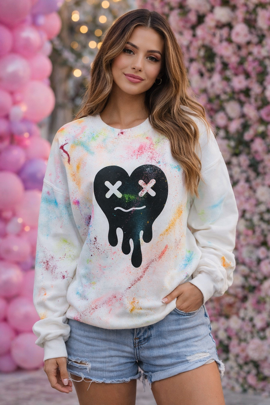 Woman wearing a colorful handpainted sweatshirt with a black heart design, standing in front of pink balloons and floral decorations.
