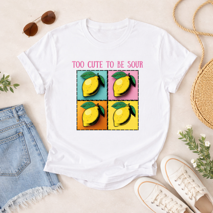 White t-shirt with lemon graphic and text 'Too Cute to be Sour' on a light background with casual items.