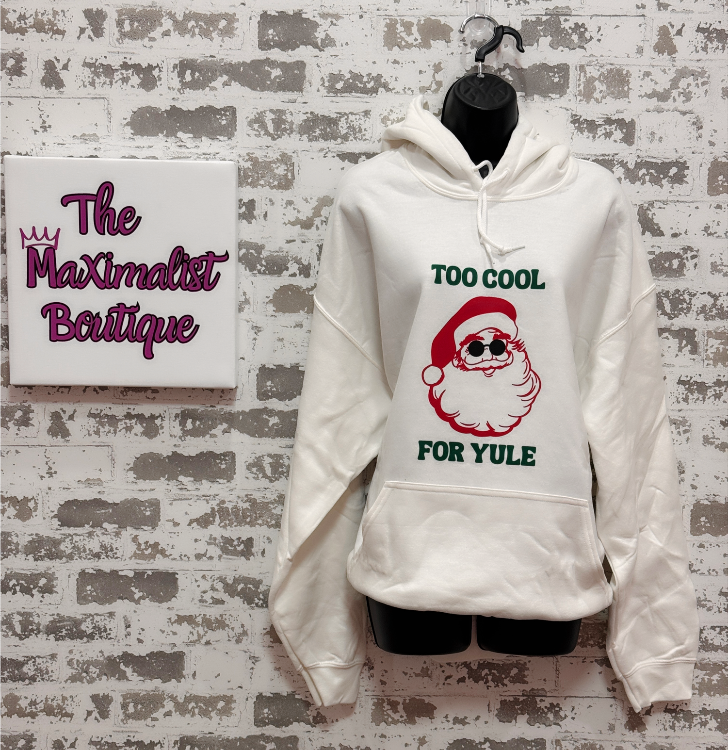 White hoodie with Santa Claus graphic and text 'Too Cool for Yule' on a textured wall background.