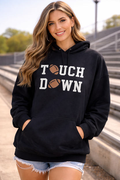 Woman wearing a black hoodie with 'Touchdown' text and a football graphic outdoors.