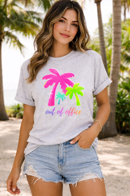Woman wearing a gray t-shirt with colorful palm tree design and 'out of office' text, standing in a tropical setting.