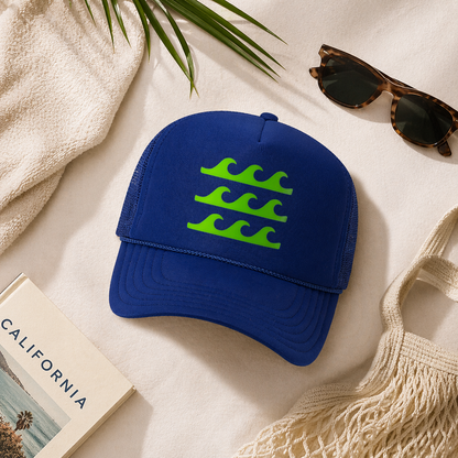 Blue cap with green wave design on a light surface with sunglasses and a towel.