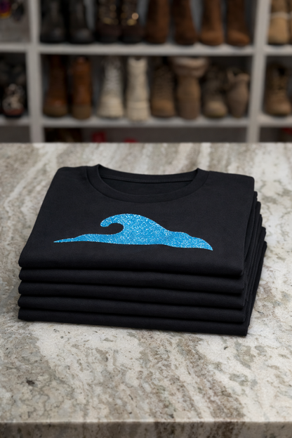 Stack of black shirts with a blue logo on a marble surface, with shoes in the background.