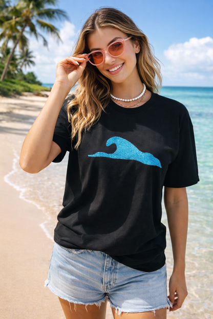 Woman wearing a black t-shirt with a blue wave design on a beach.