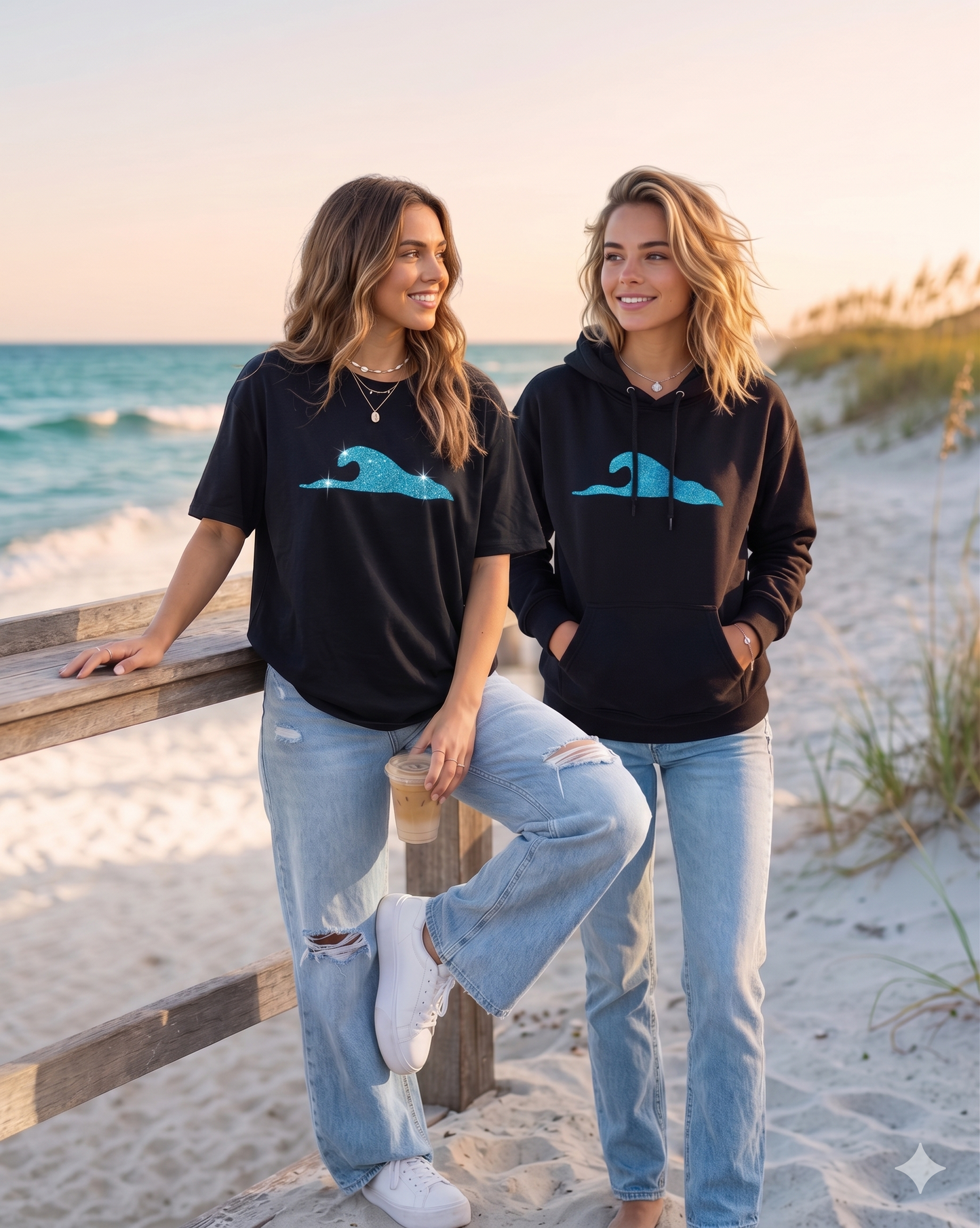 Two women standing on a beach wearing black shirts with blue wave designs.