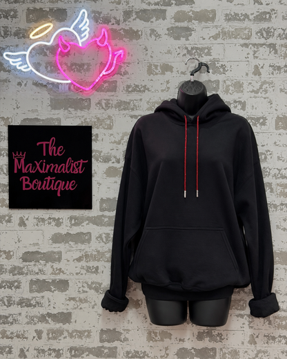 A black pullover hoodie displayed on a black mannequin torso against a faux brick wall. The hoodie has red drawstrings and a front kangaroo pocket.