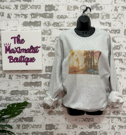Gray sweatshirt featuring a vintage postcard-style palm tree scene with the phrase “wish I was here” in the bottom left corner