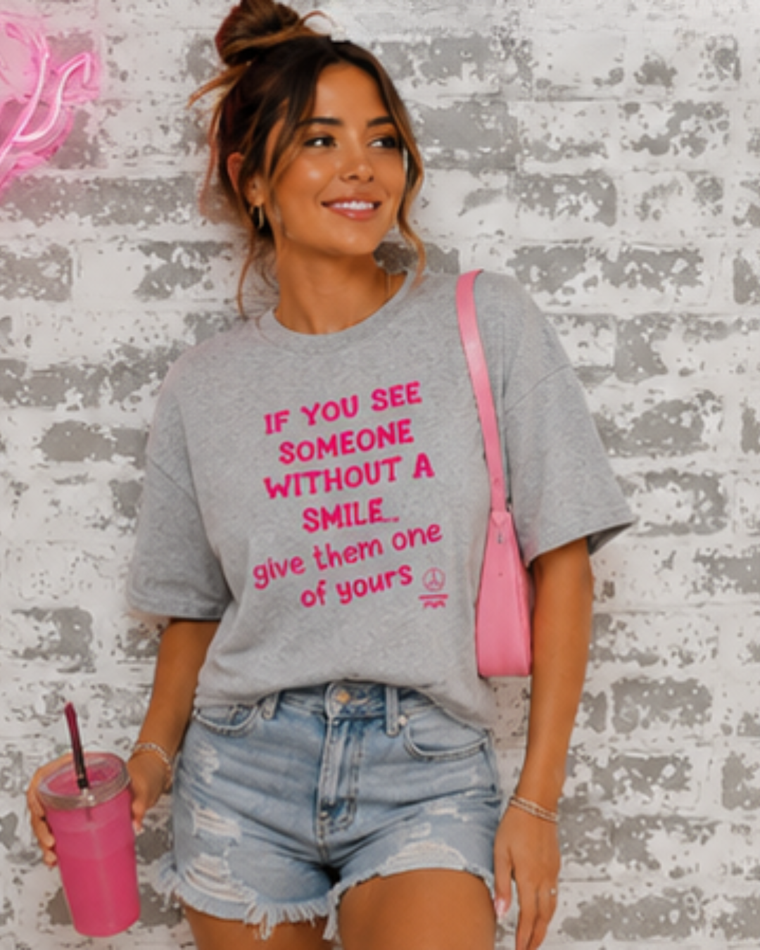 Woman wearing a gray t-shirt with a pink message, standing against a textured wall.