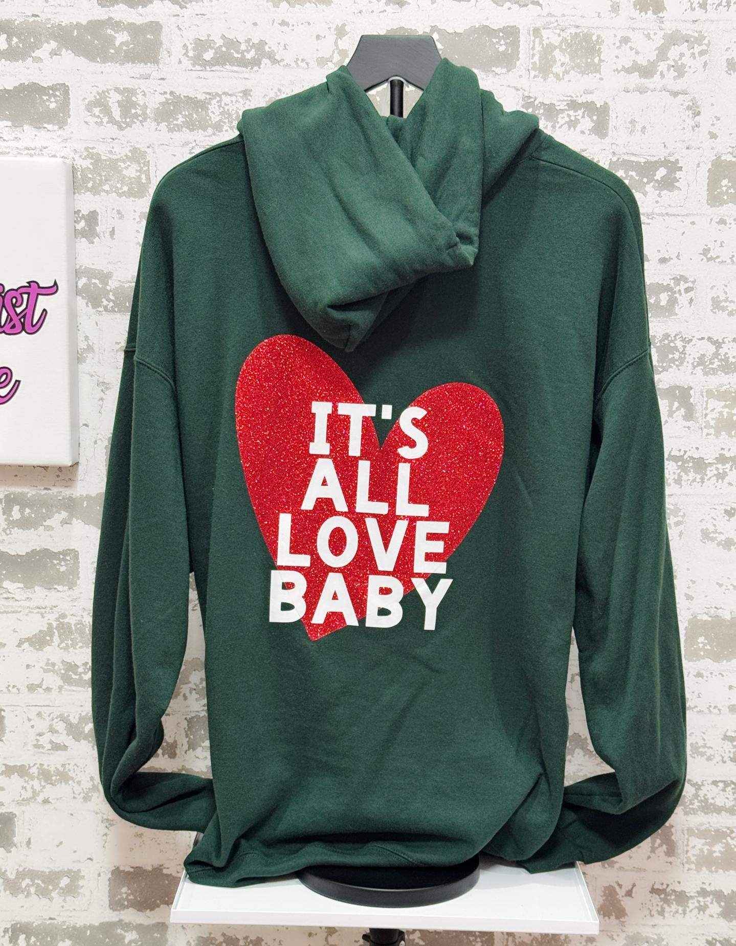 Green hoodie with red heart and text on a textured white background