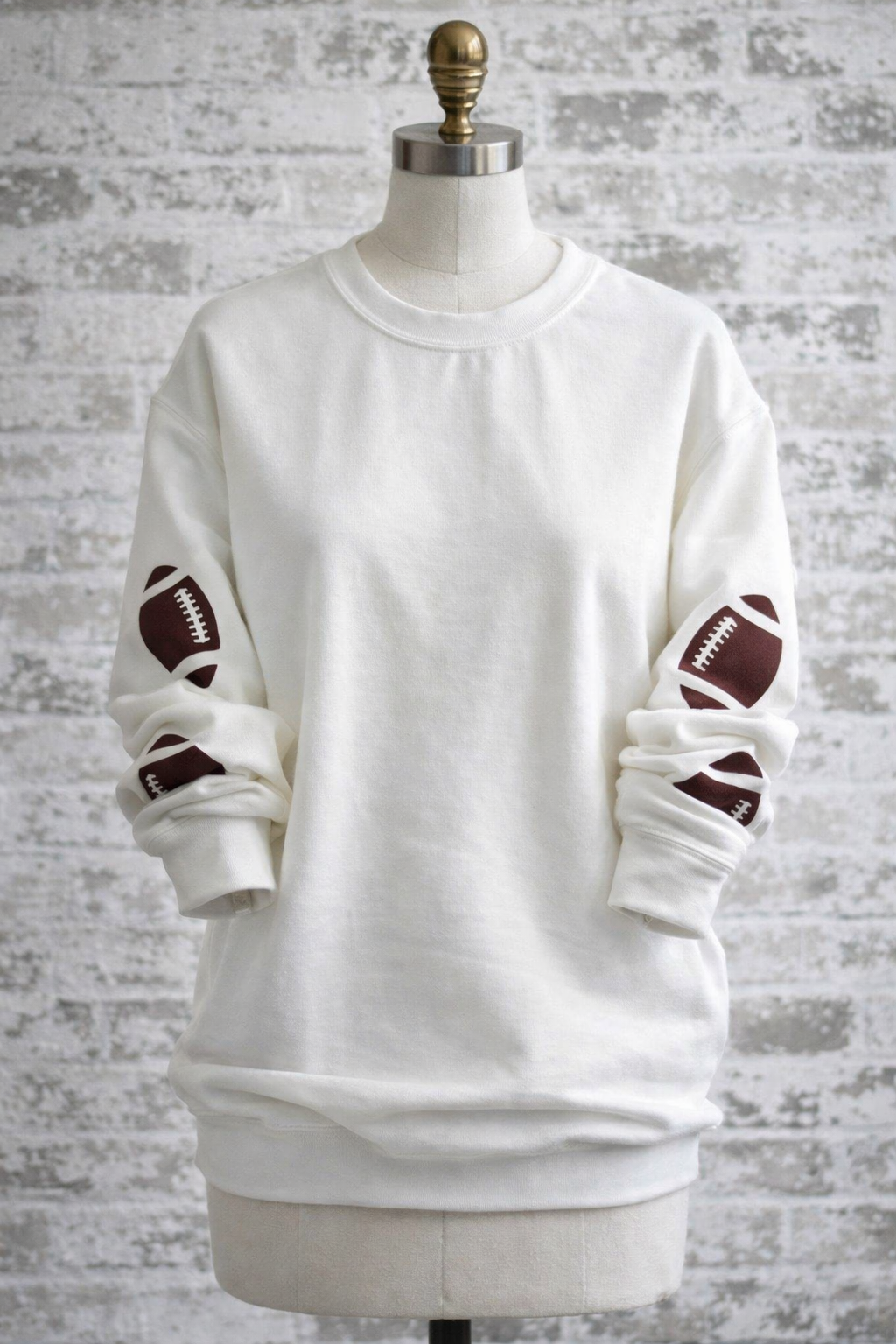 White sweatshirt with brown footballs on a mannequin against a textured gray background