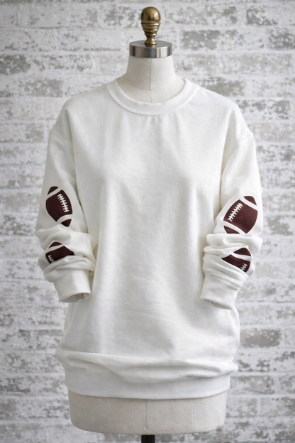 White sweatshirt with brown footballs on a mannequin against a textured gray background